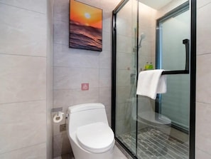 Et moderne badeværelse med glasvæg omkring bruseniche, toilet og væghængt håndvask.