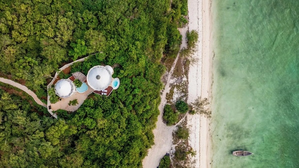 An aerial view of a resort with two dome-shaped structures, a beach, and a boat. - Kilindi Zanzibar (Kendwa)