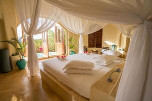 Un dormitorio con cama, mesita de noche, lámpara y vistas al exterior.
