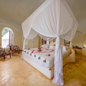 A four-poster canopy bed with a heart-shaped arrangement of red rose petals on the bedspread. - Kilindi Zanzibar (Kendwa)