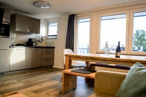 Eine moderne Küche mit Holzboden, einem Esstisch mit einer Bank und Blick durch große Fenster.