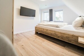 Ein Schlafzimmer mit einem hölzernen Bett, einem flachbildfernseher an der Wand und zwei Fenstern mit Vorhängen.