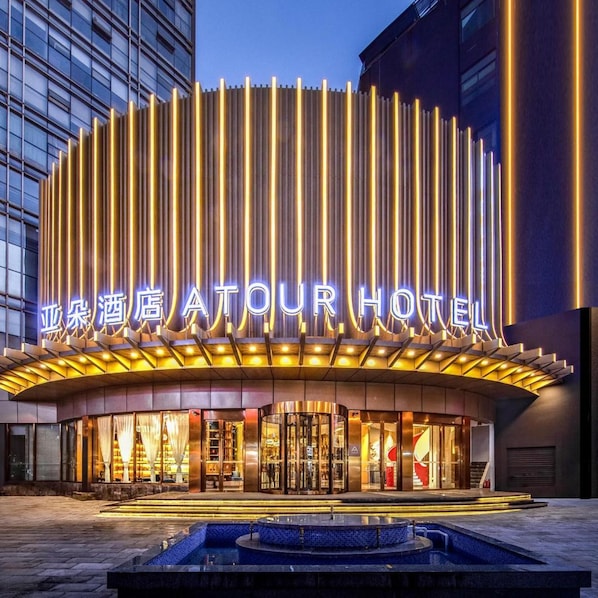 Ein Hotel mit moderner Fassade, beleuchteter Beschilderung und einem zentralen Innenhof mit Springbrunnen.