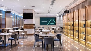 A modern dining area with tables and chairs, a large screen displaying a logo, and a patterned wall. - Atour Hotel Kunming International Trade Center (Kunming)