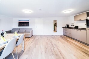 Eine moderne Küche mit Holzboden, eine Essecke mit Tisch für zwei Personen und ein graues Sofa.