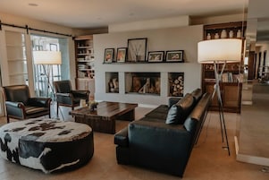 Una sala de estar con chimenea, muebles de cuero, una mesa de centro y una estantería.