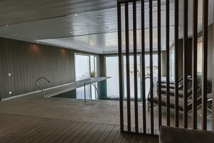 Un área de piscina interior moderna con cubierta de madera, barandilla de metal y vistas al exterior.