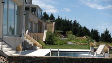 Una casa moderna con piscina, mobiliario exterior y una escalera que conduce a un balcón.