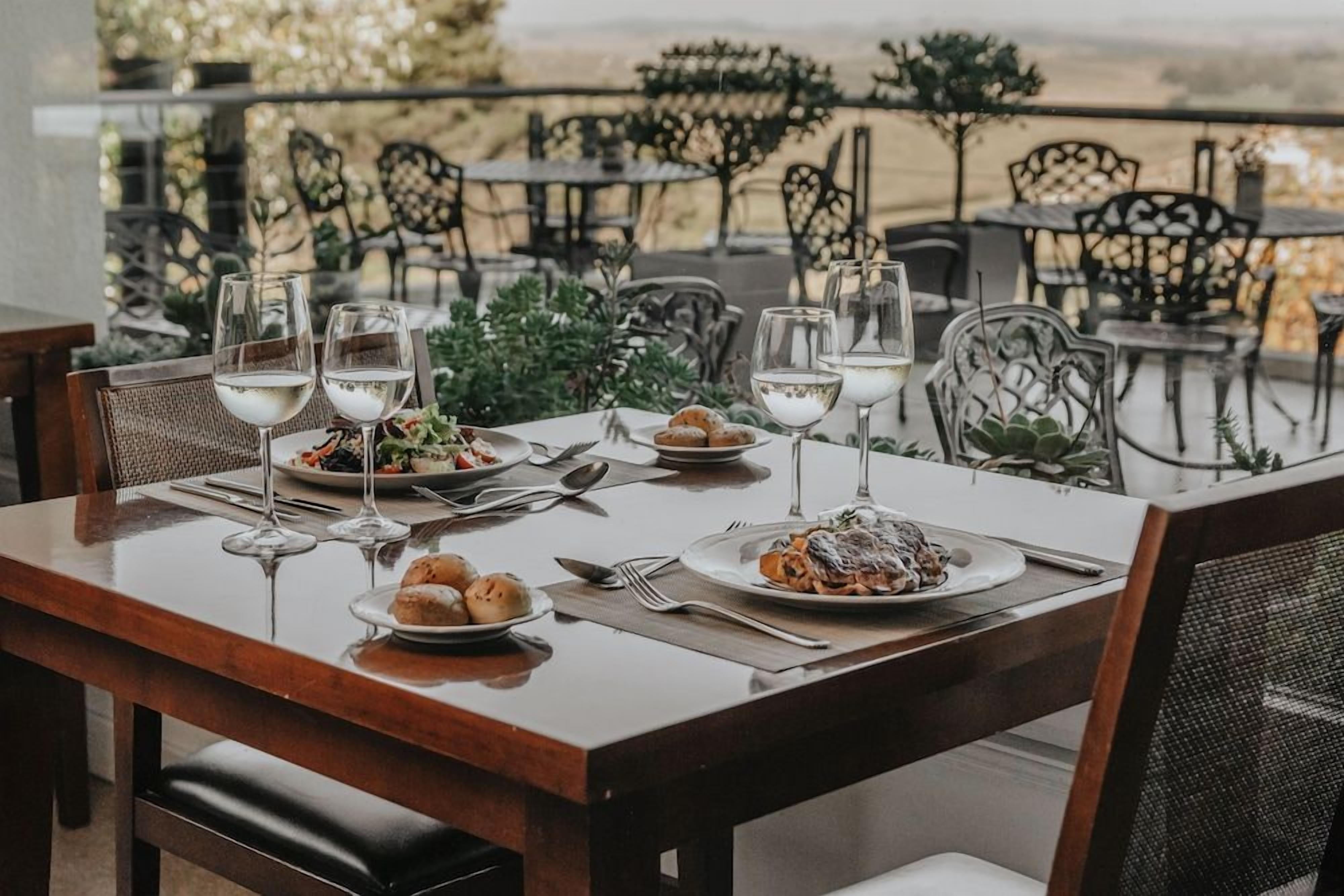 Un área de comedor al aire libre con mesas dispuestas para una comida, rodeada de sillas y plantas.