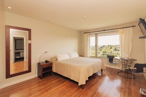 Un dormitorio con cama, escritorio y silla, ventana con vistas, y espejo en la pared.
