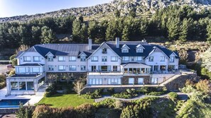 Ein großes, mehrstöckiges Haus mit Schwimmbecken, umgeben von einem angelegten Garten und einer bergigen Landschaft.