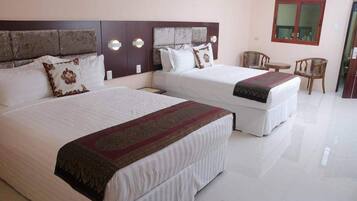 A hotel room with two beds, a wooden headboard, a small table with chairs, and a window.