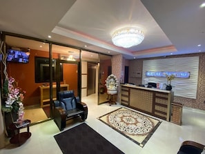 A hotel lobby with a reception desk, a chandelier, a television, and a decorative statue. - Grand Diamond Hotel (Piarco)