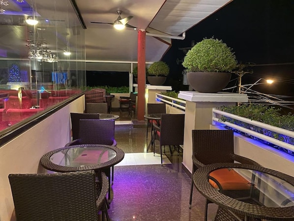 An outdoor balcony with wicker furniture, potted plants, and a glass railing. - Grand Diamond Hotel (Piarco)