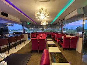 A restaurant with red upholstered booths, a bar area, and a chandelier. - Grand Diamond Hotel (Piarco)
