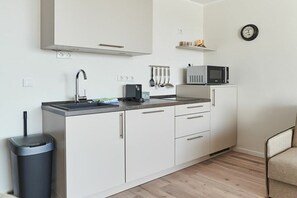 Eine kleine Küche mit weißen Schränken, einer Edelstahl-Spüle und einer Mikrowelle auf der Arbeitsplatte.