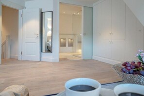 Ein modernes Interieur mit Holzboden, einer weißen Tür und Blick in ein Schlafzimmer mit Bett und Nachttisch.