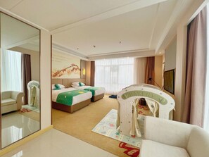 Habitació d'hotel amb un mirall gran, un llit amb roba de llit verda, un sofà, una zona de jocs i una televisió.