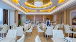 A hotel dining area with white chairs and tables, a central serving station, and a chandelier. - Vienna International Hotel (Wuhan)