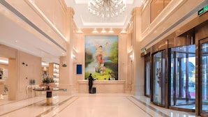 A spacious lobby with a large mural, a chandelier, and a glass entrance. - Vienna International Hotel (Shangqiu)