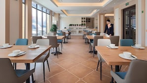 A modern dining area with tables and chairs, a reception desk, and a large window. - Vienna International Hotel (Shangqiu)