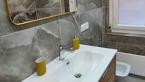 Uma casa de banho moderna com uma toucador de madeira, uma sanita branca, um espelho com moldura dourada e uma janela.