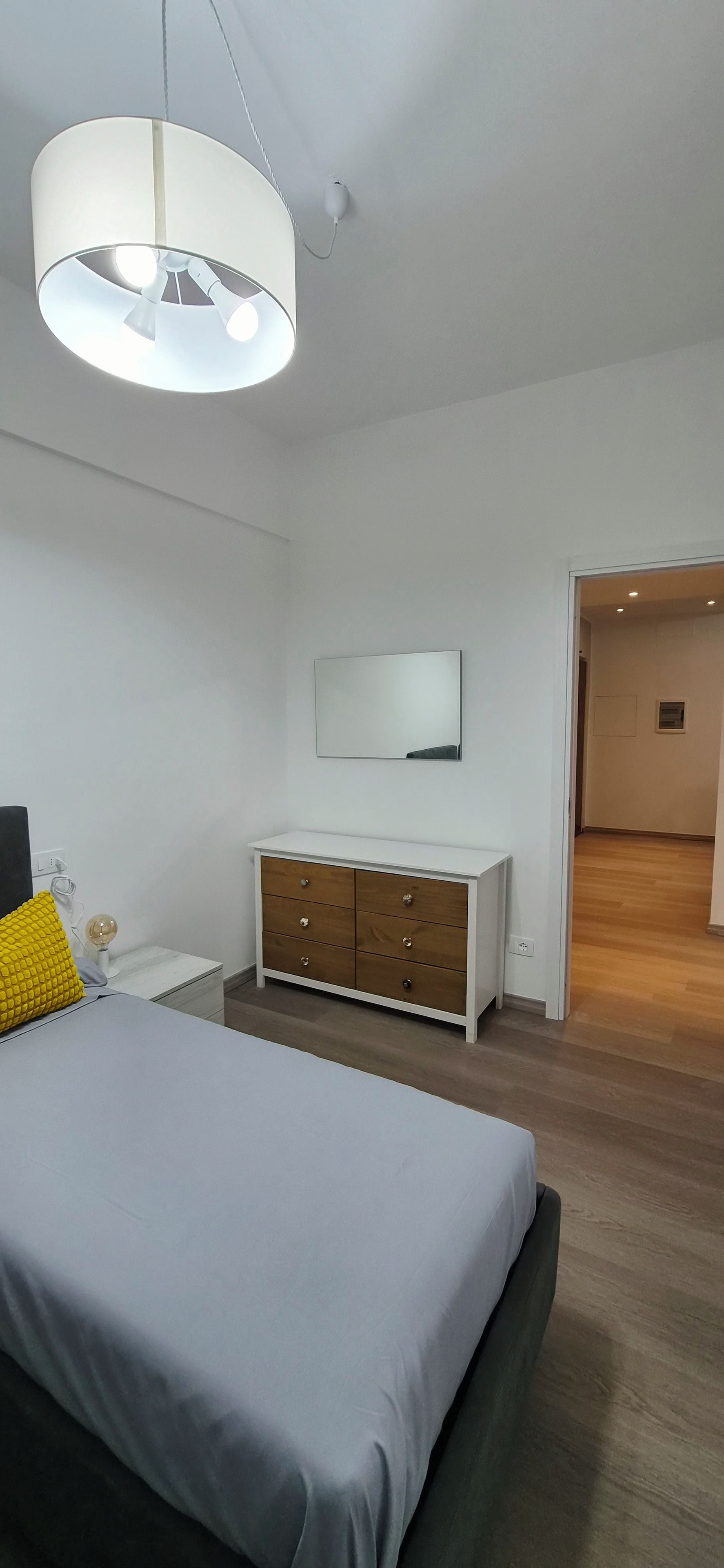 Ein Schlafzimmer mit Bett, Kommode, Spiegel und einer Deckenleuchte.