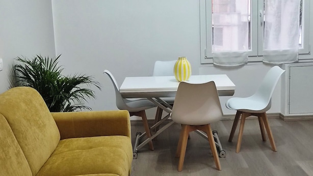 Uma sala de estar moderna com um sofá amarelo, uma mesa de jantar com cadeiras e uma planta em vaso.