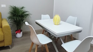 Uma área de refeições com uma mesa e cadeiras brancas, uma planta em vaso e um vaso listrado de amarelo.