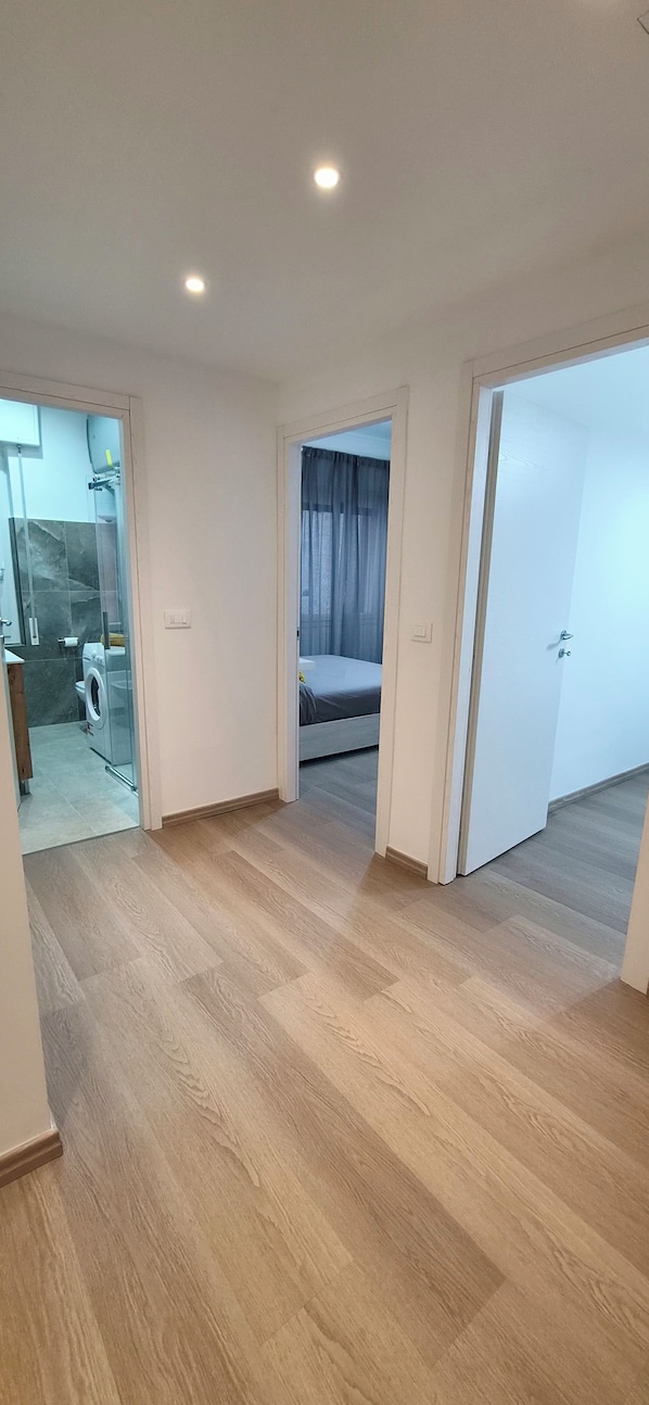 A room with a wooden floor, a bed, a washing machine, and a glass shower enclosure.