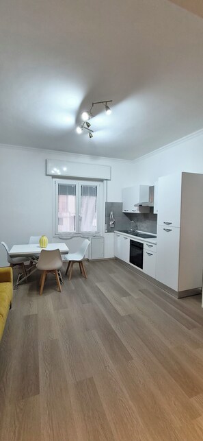 A modern kitchen with white cabinets, a dining area with a table and chairs, and a yellow sofa.