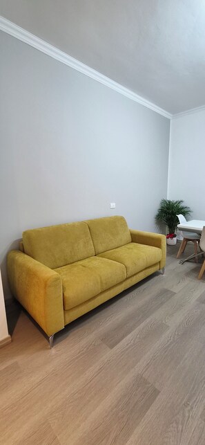 Et værelse med en gul sofa, et hvidt bord og en potteplante.