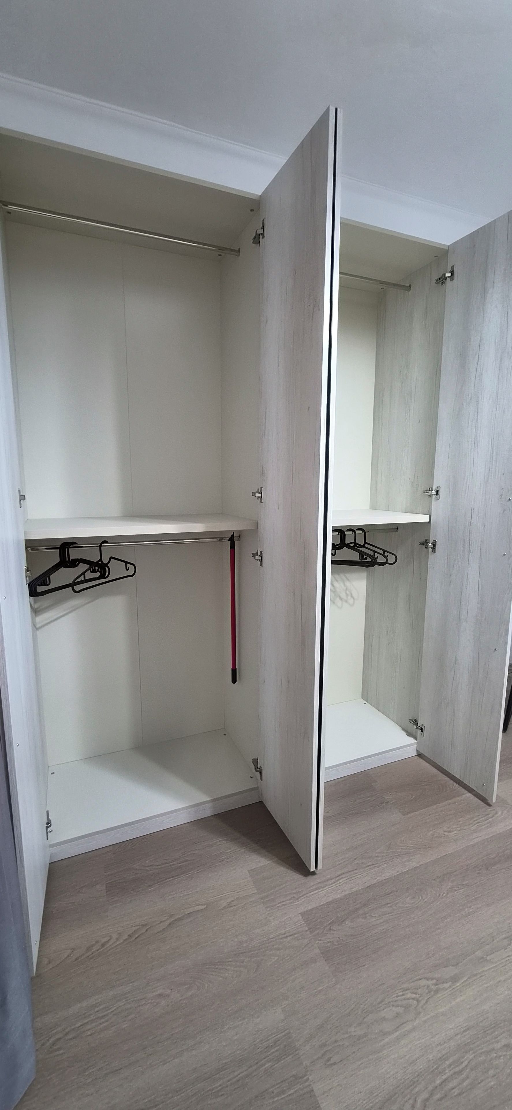 Ein begehbarer Kleiderschrank mit offenen Türen, Holzboden und Metallkleiderbügeln.