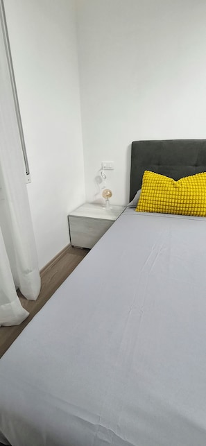 Un dormitori amb llit, una tauleta de nit, una làmpada i una presa corrent.
