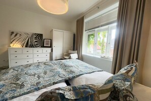 A bedroom with a bed, a dresser, a window with curtains, and a ceiling light. - Holiday apartment in Föhr with 2 bedrooms (Wyk auf Föhr)