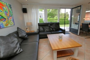 Ein modernes Wohnzimmer mit einer Ledersofa, einem Holztisch und einem großen Fenster mit Blick auf den Garten.