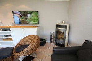 A living room with a television, a fireplace, a wicker chair, a black sofa, and a white cabinet. - Schmalstieg 11a, Wyker Perle (Wyk auf Föhr)