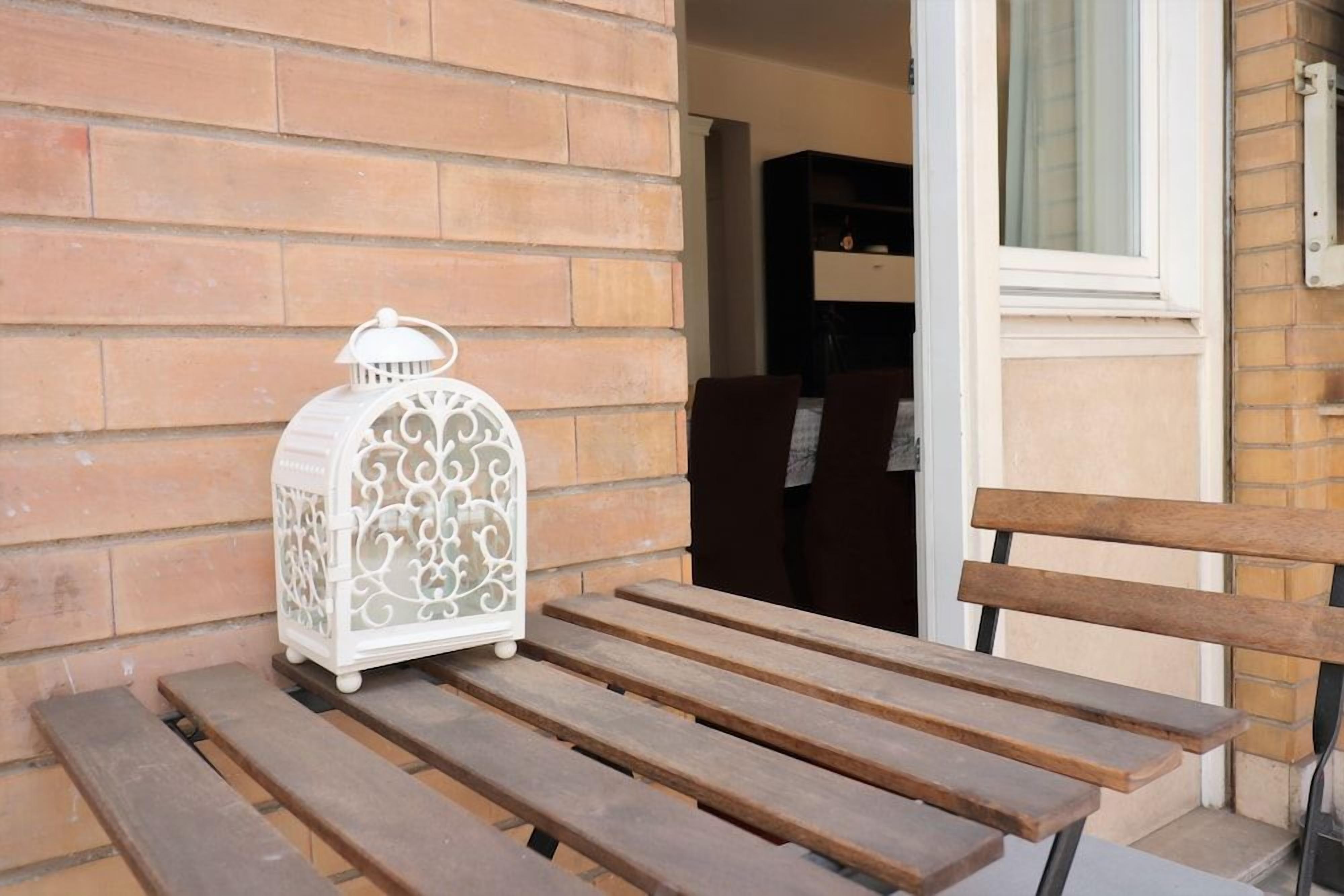 A wooden bench with a white lantern beside it, against a brick wall.