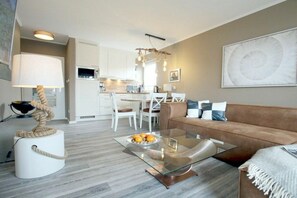 A modern living room with a glass coffee table, a brown sofa, and a dining area with white chairs. - E2 "Nordmeer" at Feldstr. 18 (Wyk auf Föhr)