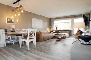 Een moderne woonkamer met een bruine bank, een eettafel met stoelen, een bijzettafeltje en een televisie op een meubel.