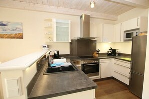 A modern kitchen with white cabinets, a stainless steel range, a microwave, and a refrigerator. - Seeschwalbe at Susanne-Fischer-Weg 49 (Wyk auf Föhr)