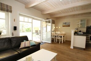 Een moderne woonkamer met een zwarte leren bank, een witte salontafel en een eethoek met witte stoelen en een tafel.