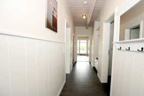 A hallway with white wainscoting, a dark floor, and a door at the end leading to a bright room. - Seeschwalbe at Susanne-Fischer-Weg 49 (Wyk auf Föhr)