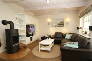 A living room with a black wood-burning stove, a white entertainment unit with a TV, a brown leather sofa, and a white coffee table. - Seeschwalbe at Susanne-Fischer-Weg 49 (Wyk auf Föhr)