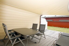 A covered outdoor area with a table and chairs, a view of a red building, and a grassy area. - Shrimp in Susanne-Fischer Weg 33 (Wyk auf Föhr)