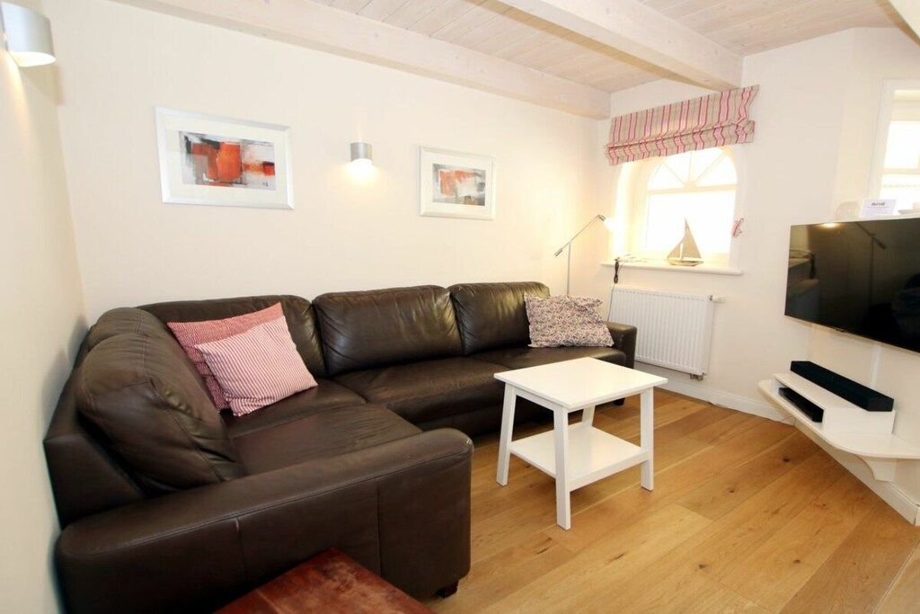 Un salon moderne avec un canapé en cuir, une table basse blanche et un téléviseur à écran plat fixé au mur.