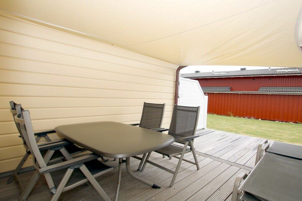 A covered outdoor area with a table and chairs, a view of a red building, and a grassy area.