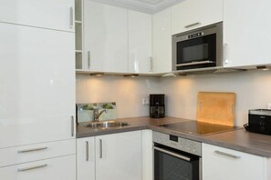 Una cocina moderna con armarios blancos, microondas integrado, cafetera y tostadora.