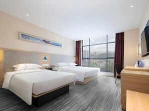 Habitación de hotel con dos camas, un escritorio y un ventanal con vistas a la ciudad.
