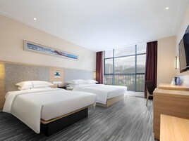 Habitación de hotel con dos camas, un escritorio y un ventanal con vistas a la ciudad.